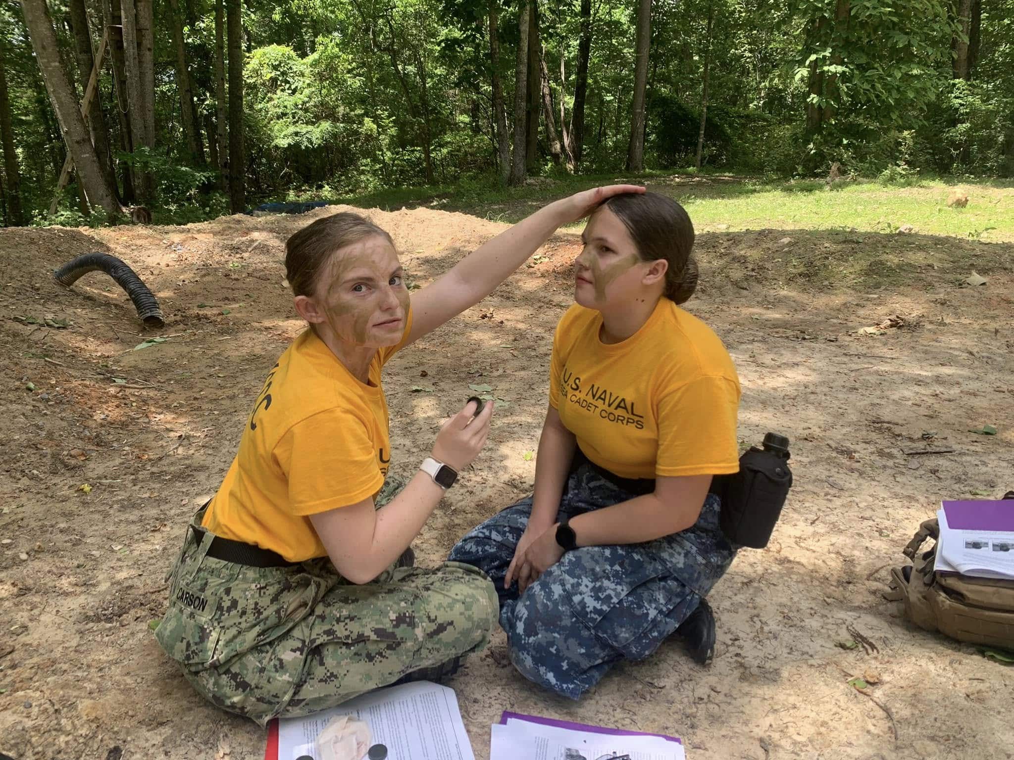 Two female cadets applying camo face paint to each other