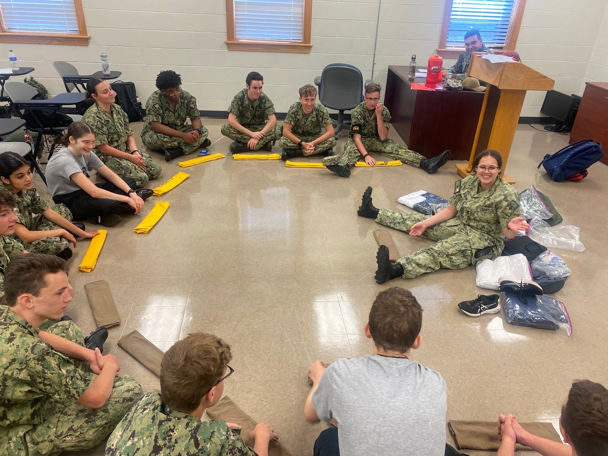 Large group of cadets seated in a circle receiving gear during drill
