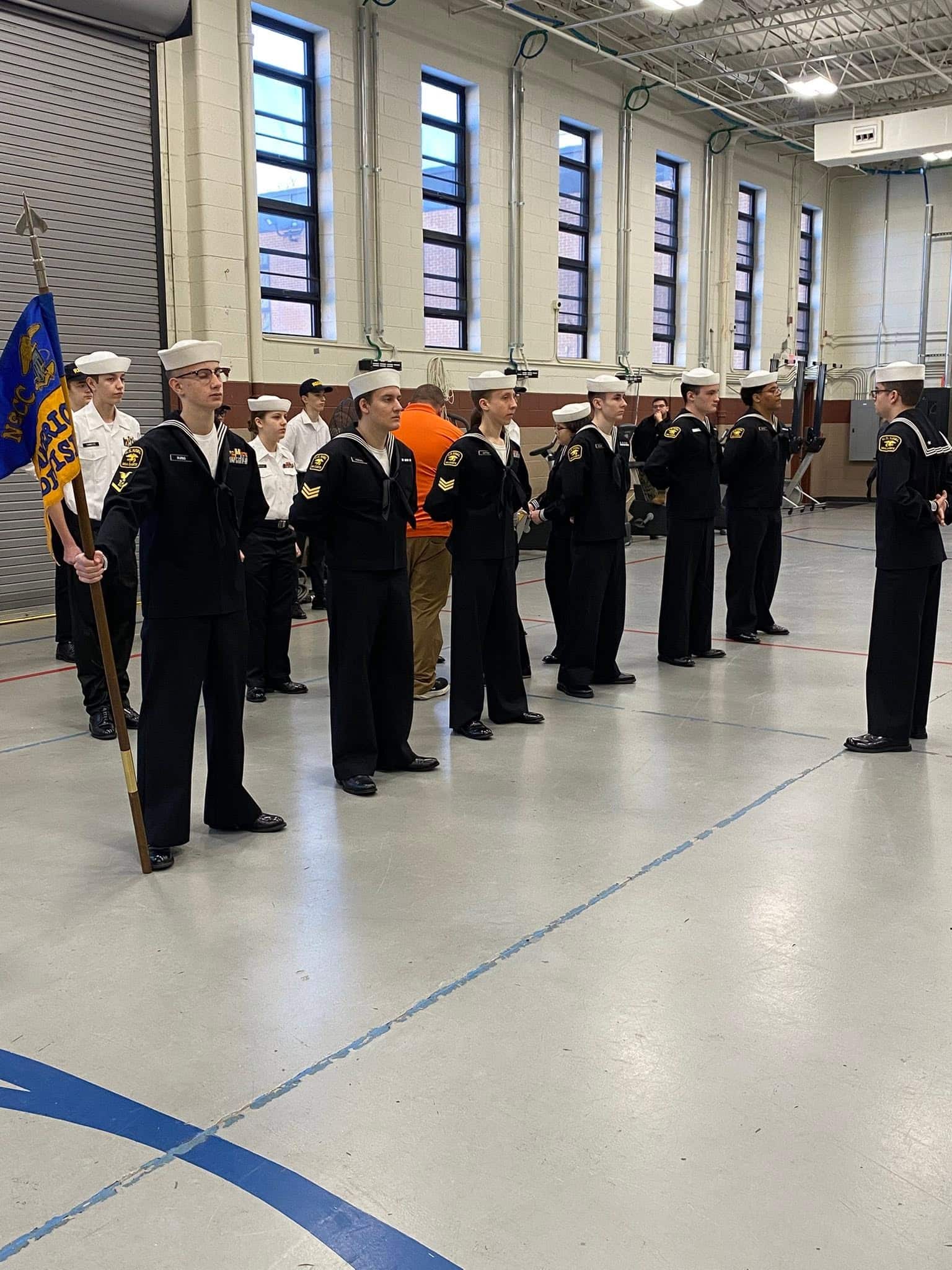 Cadets in dress blues in indoor formation with unit flag