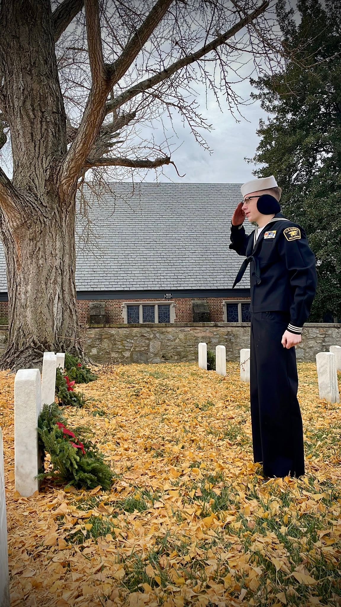 Cadet in dress blues saluting at a grave in a cemetery