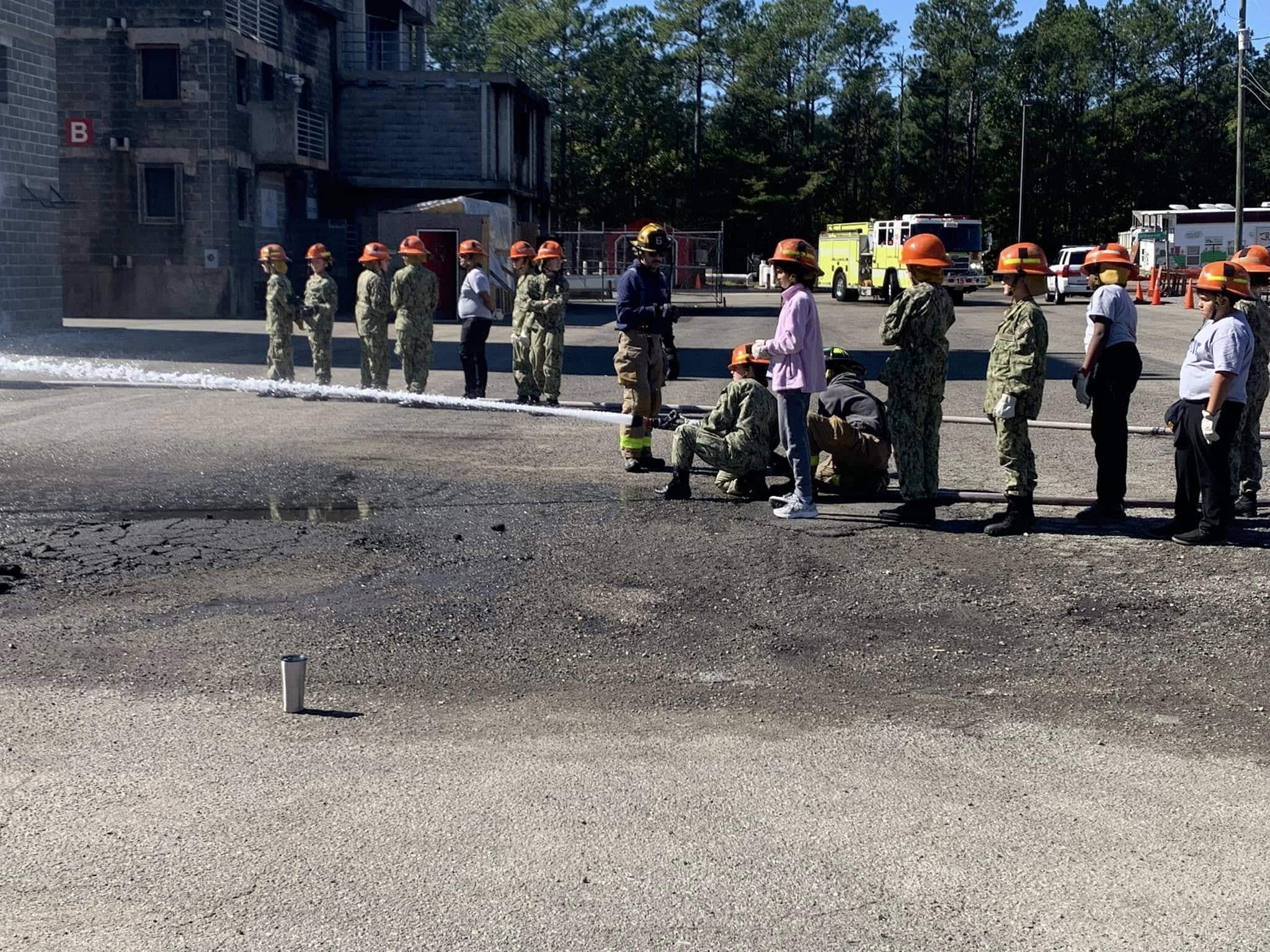 Cadets in hard hats operating a fire hose at a live training facility