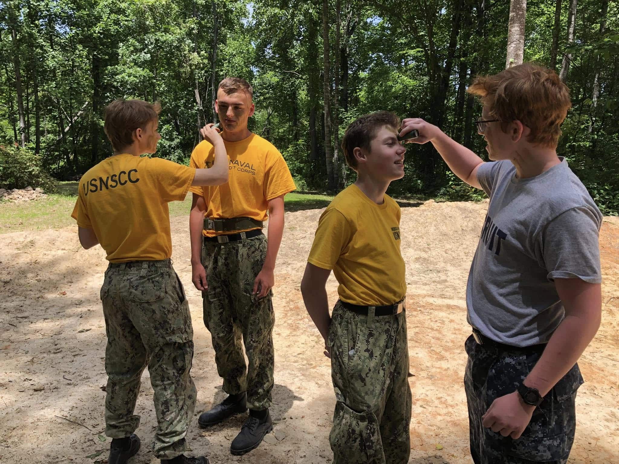 Four cadets applying camouflage face paint outdoors