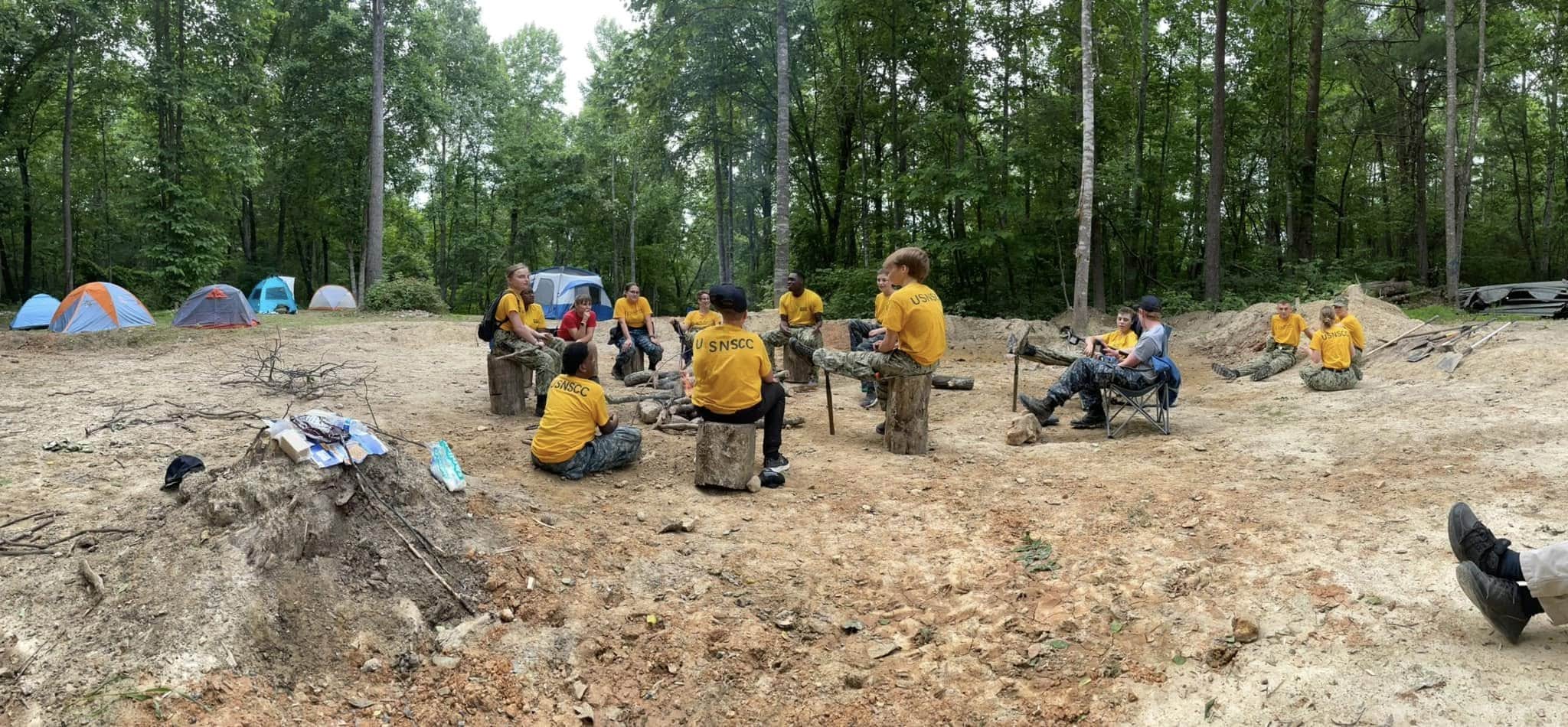 Wide shot of cadets seated in a circle at a campsite